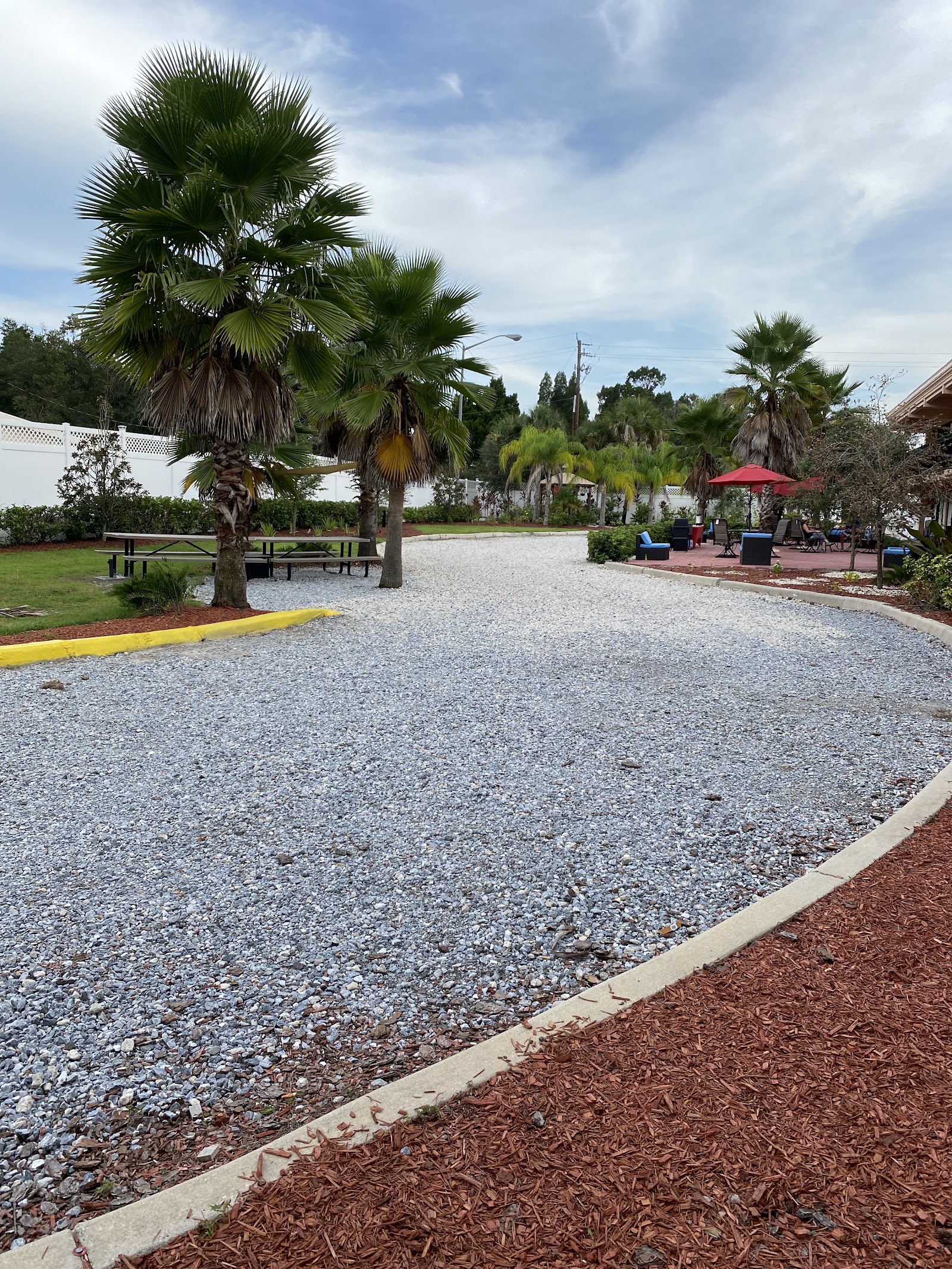 Exterior outdoor grounds with palm trees, picnic tables, seating areas, and red umbrella in landscaped recreational space