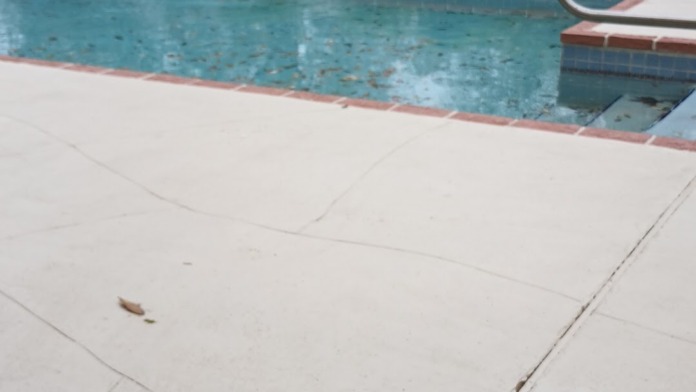 Outdoor swimming pool with concrete deck, metal railing, and brick edging surrounding water
