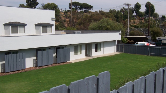 Exterior view of facility grounds showing manicured lawn, fenced perimeter, and modern white building with multiple windows
