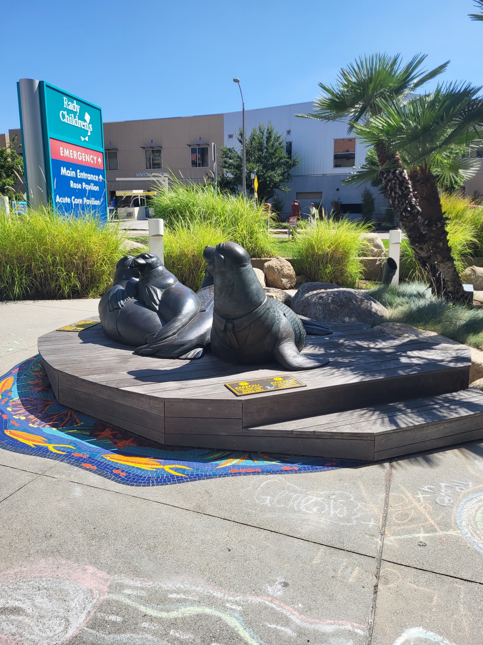 Outdoor plaza featuring large seal sculptures, colorful mosaic artwork, palm trees and landscaping
