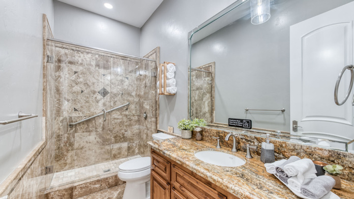 Interior bathroom with walk-in shower enclosure, vanity sink, granite countertop, and wooden accents