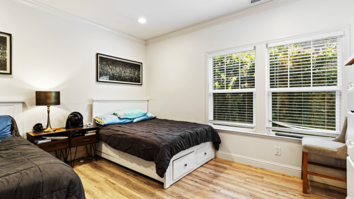 Interior bedroom with twin beds, wooden nightstand with lamp, large windows with shutters, hardwood floors