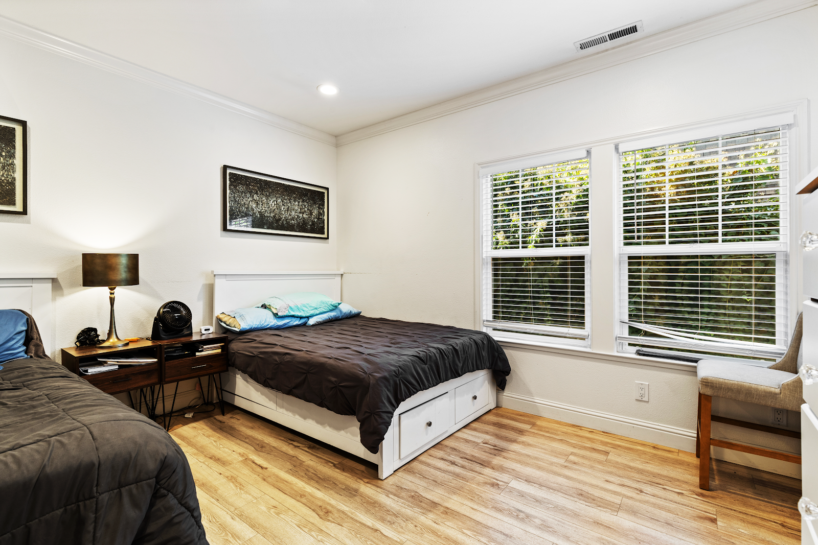 Interior bedroom with twin beds, wooden nightstand with lamp, large windows with shutters, hardwood floors