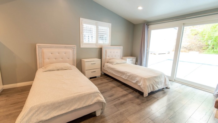 Interior bedroom with two single beds, wood flooring, nightstand, and sliding glass door to outdoor area.