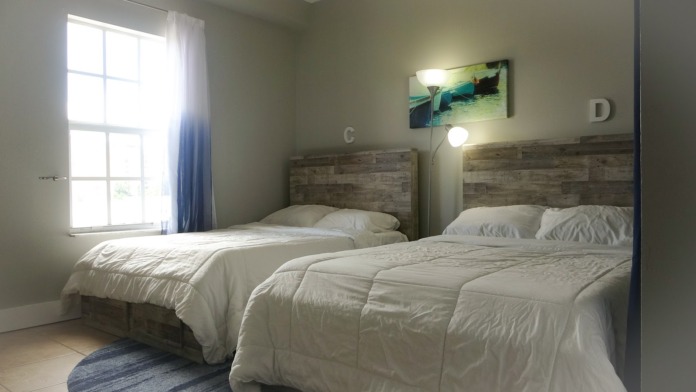 Interior patient bedroom with two beds, wooden headboards, pillows, and natural light from window with curtains