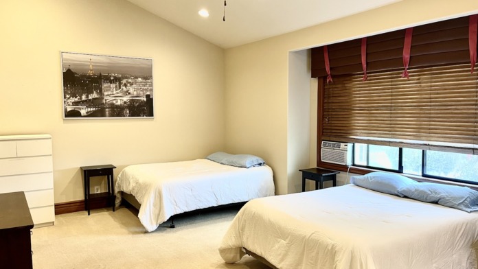 Interior bedroom with two beds, window with wood blinds, nightstands, and comfortable furnishings