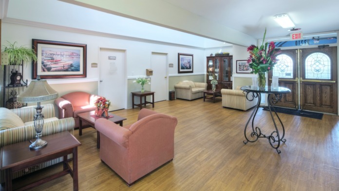 Interior patient room with two beds, medical equipment overhead, natural light from windows with blinds, wood flooring