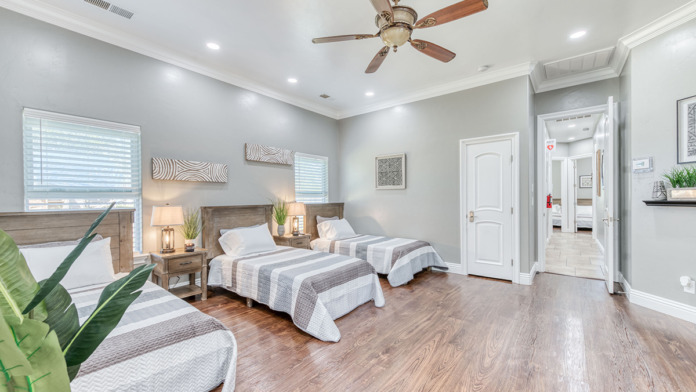 Interior patient bedroom suite with three twin beds, wood furnishings, windows, and comfortable bedding