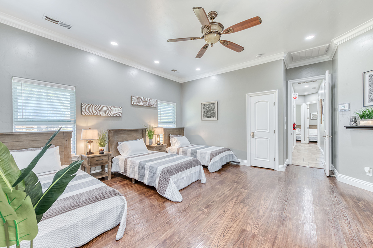 Interior patient bedroom suite with three twin beds, wood furnishings, windows, and comfortable bedding