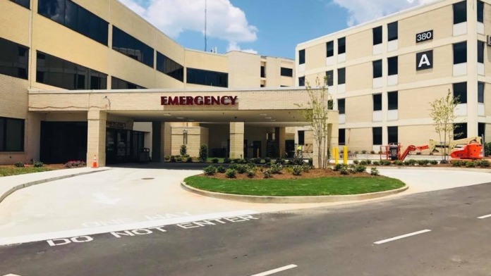 Interior patient room with hospital bed, comfortable seating, bassinet, medical equipment, and windows with natural light