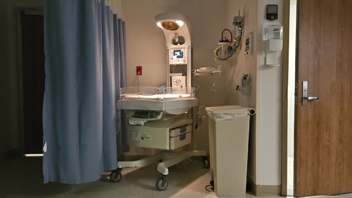 Interior patient sink vanity with mirror, faucet, towel dispenser, wall-mounted medical equipment, oxygen ports, and hospital-grade finishes.