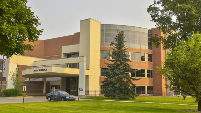 Exterior view of behavioral health facility showing patient entrance with yellow and cream canopy, red brick construction, multiple windows, and landscaped grounds