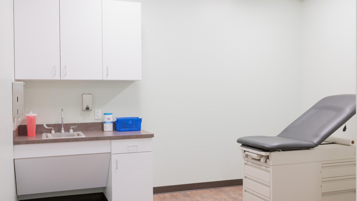 Examination room with white cabinetry, sink, medical chair with gray pad, storage furniture, clinical setup