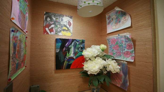 Interior hallway with wood-textured walls, multiple patient room doors, artwork displays, and decorative vase