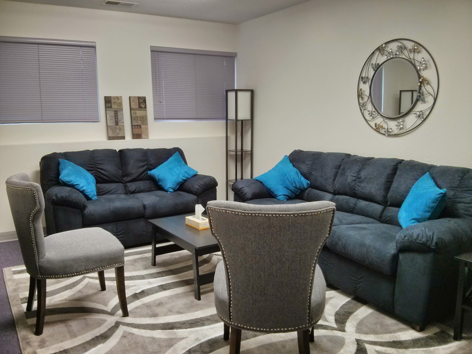 Interior lounge space with two black sofas, blue accent pillows, small table, and patterned area rug.