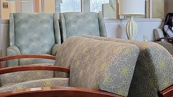 Interior lounge space with upholstered chairs and seating, decorative wood trim, glass partition windows, lamp, and modern furnishings for patient relaxation