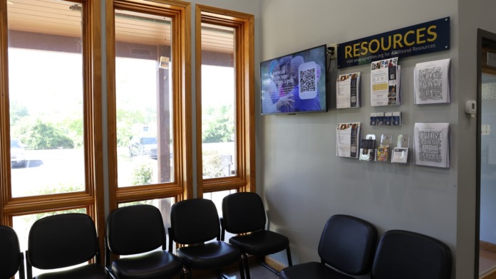 Interior waiting room with black padded seating chairs, natural lighting from multi-paned windows, and resource information displays