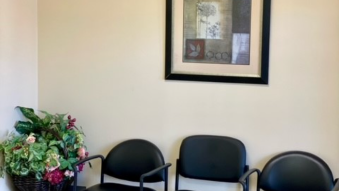 Interior waiting room with comfortable seating, potted plant, framed artwork, and beige walls with carpeted flooring