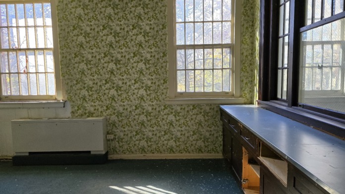 Interior room with green floral wallpaper, windows with security bars, built-in bench, and natural light.