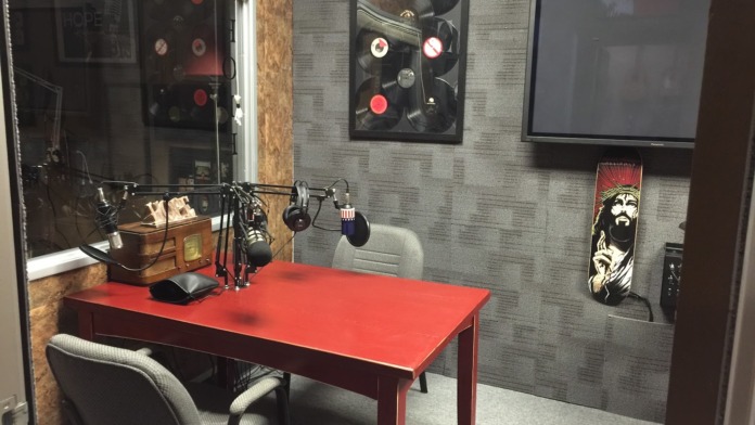 Interior media studio with red table, professional microphone, gray textured walls, and decorative artwork