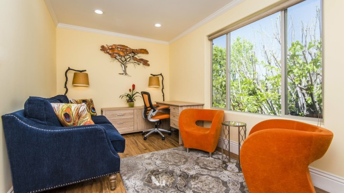 Interior office space with yellow walls, blue and orange modern seating, desk area and large windows