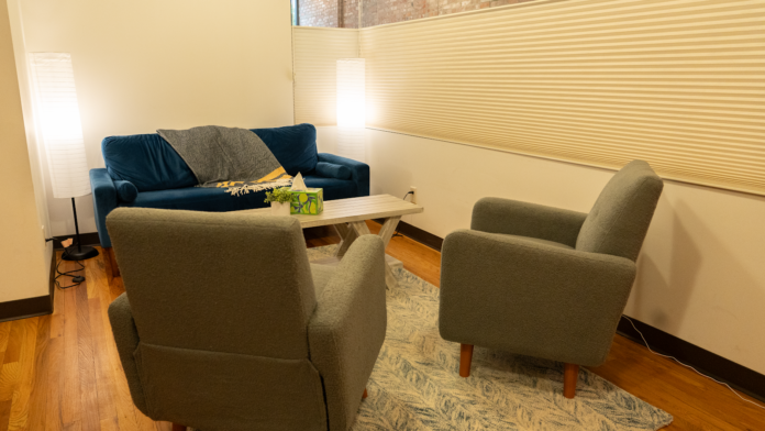Interior therapy room with blue and gray seating, coffee table, wooden flooring, and cream walls