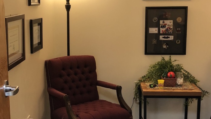 Interior room with burgundy upholstered chair, side table, decorative plants, framed art, and warm accent lighting.