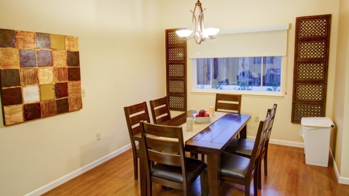 Interior dining space with wooden table and chairs, decorative wall art, pendant lighting, large windows, and decorative shelving