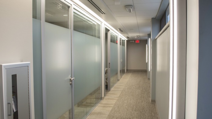 Interior hallway with frosted glass-walled private offices or consultation rooms lining both sides, bright lighting.