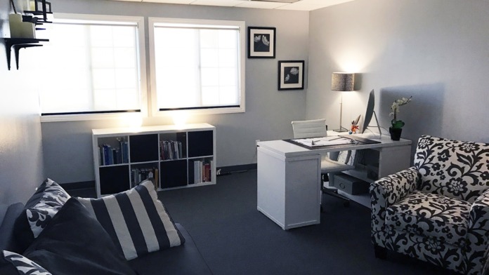 Interior office space with patterned upholstered chair, floating desk with computer, bookshelf, and natural lighting from windows