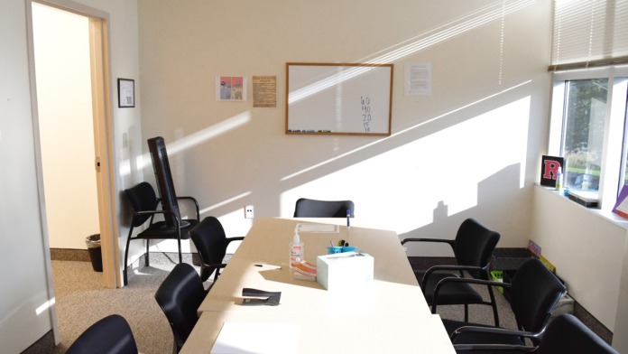 Interior meeting space with long white table, black chairs, whiteboard, and bright windows.