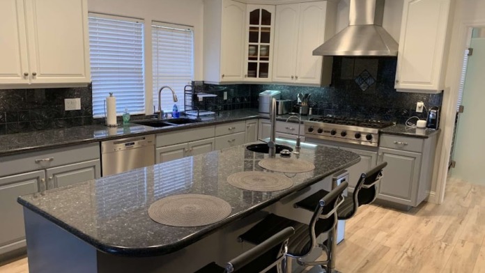 Interior kitchen with white cabinetry, black granite counters, stainless steel appliances, island seating, gas range