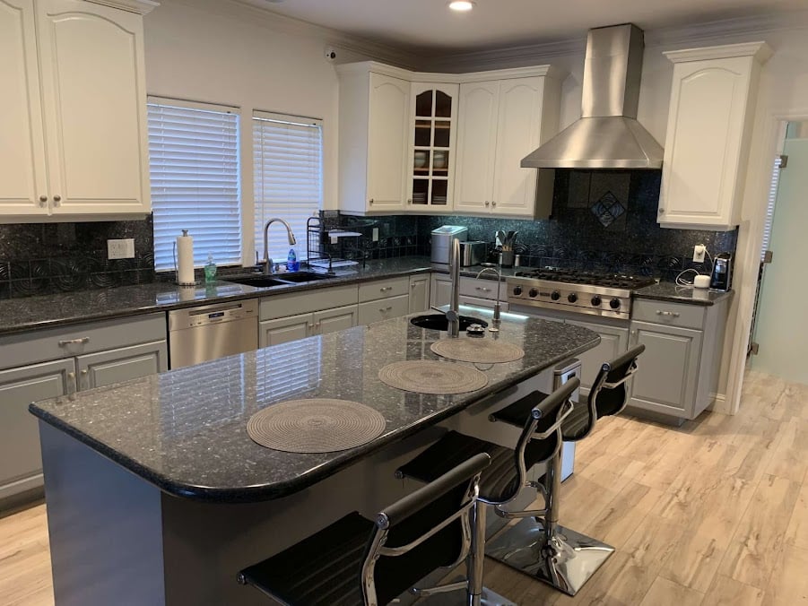 Interior kitchen with white cabinetry, black granite counters, stainless steel appliances, island seating, gas range