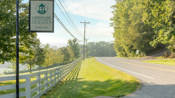 Exterior showing Cumberland Heights facility signage on pole post, white fencing, and tree-lined approach road