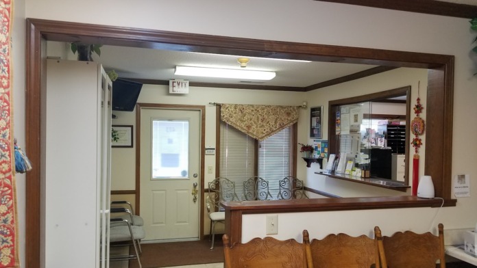 Interior reception area showing wooden-framed service counter, cream-colored entry door, beige walls, and administrative workspace with office furnishings.