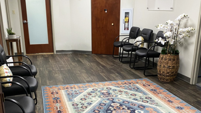 Interior reception area with dark wood doors, wall clock, High Focus signage, black client chairs, decorative rug, and woven planter.