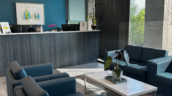 Interior reception area with teal accent wall, dark desk, black seating, and large windows with blinds