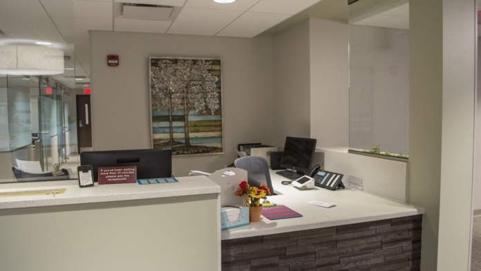 Interior reception counter with white surface, desktop computers, office materials, and potted plant decoration.