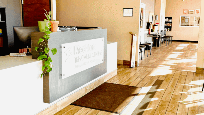Interior reception area with MedMark Treatment Centers signage on desk, pendant lighting, plants, and clear sightlines to facility interior