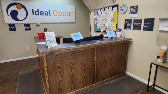 Interior reception desk with Ideal Option facility signage and informational materials posted on wall