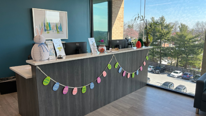 Interior reception desk area with teal wall, white counter, colorful decorations, and window overlooking parking lot