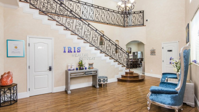 Interior foyer with grand ornate staircase, beige walls, facility name signage, decorative elements and wooden flooring