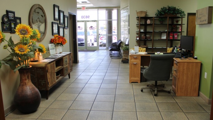 Interior reception office area with green walls, wooden furniture, desk workspace, floral arrangements, and front windows