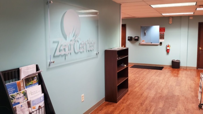 Interior reception area with Zepf Center logo on wall, wooden flooring, shelving unit, and administrative workspace with signage and documents