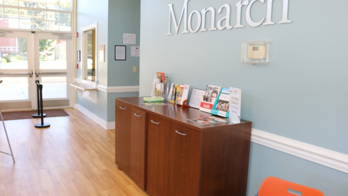 Interior reception area with Monarch signage, wooden counter desk, and welcoming lobby space with windows