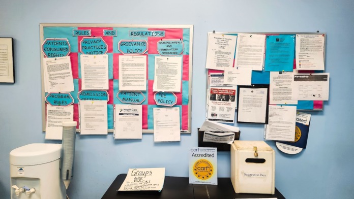 Interior wall showing colorful laminated information posters in pink and turquoise sections, water cooler, desk materials, and facility signage
