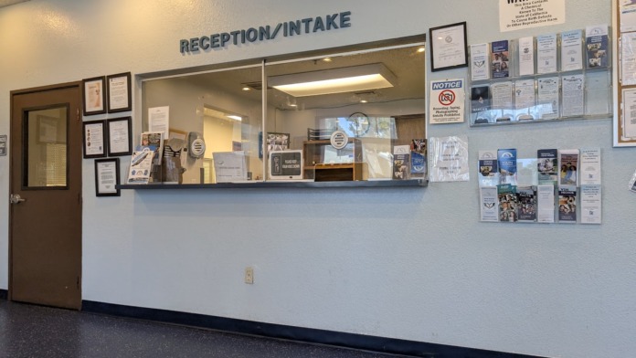 Interior reception counter with check-in window, informational postings, and waiting area seating