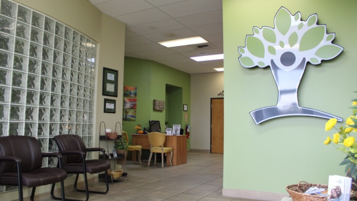 Interior reception lobby with green accent walls, glass block feature, leather seating, wooden desk, and facility logo graphic