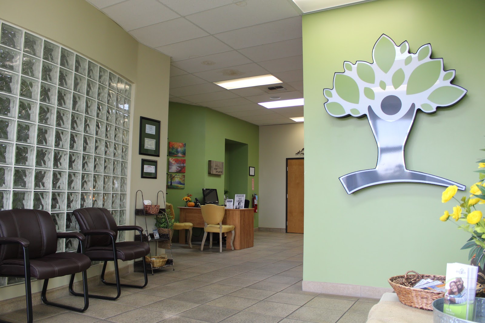 Interior reception lobby with green accent walls, glass block feature, leather seating, wooden desk, and facility logo graphic