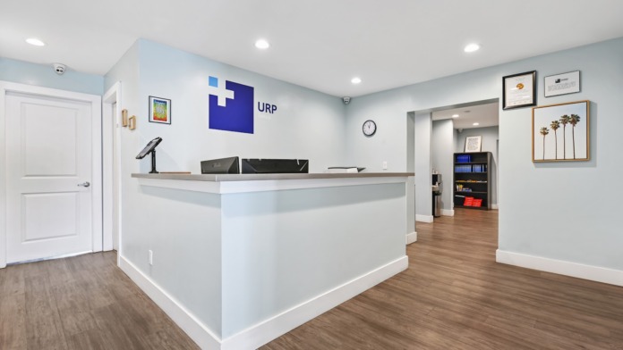 Interior reception desk with URP logo signage, modern white counter, wooden flooring, and professional facility entrance